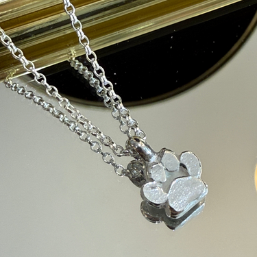 skinny wrists Silver necklace with a paw print pendant on a reflective surface