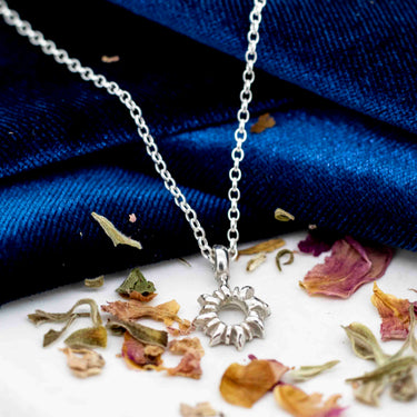 skinny wrists Silver necklace with a sunflower pendant on a blue fabric background with dried flowers.
