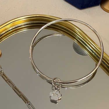 Silver bangle with a paw print charm on a reflective surface